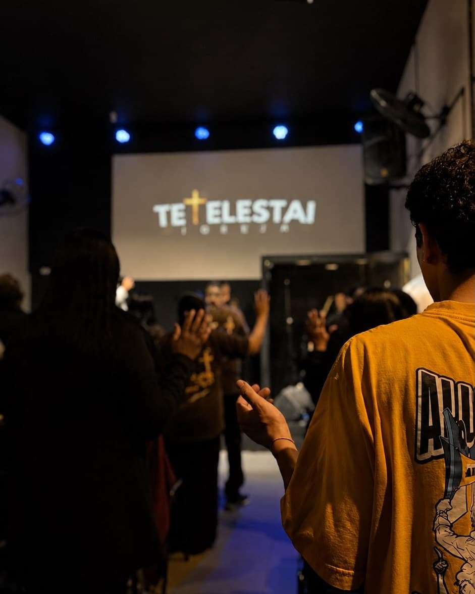 Congregação da Tetelestai Church em oração diante do telão com o nome da igreja